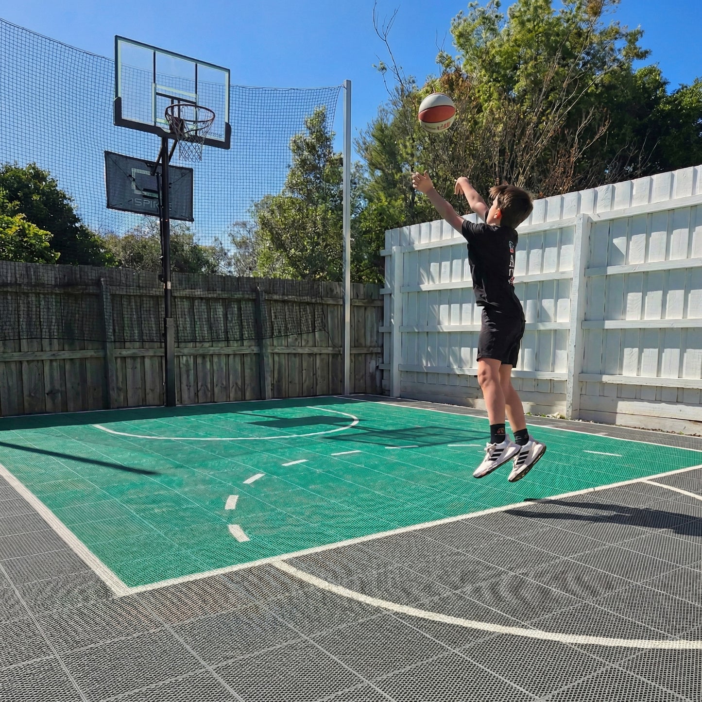 Person playing basketball on an outdoor court with green and grey Coueta tiles